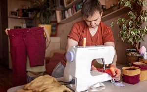 A person using a sewing machine to upcycle red jeans
