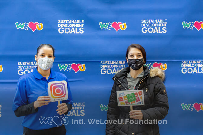 Two masked participants are holding photo props in front of a step and repeat