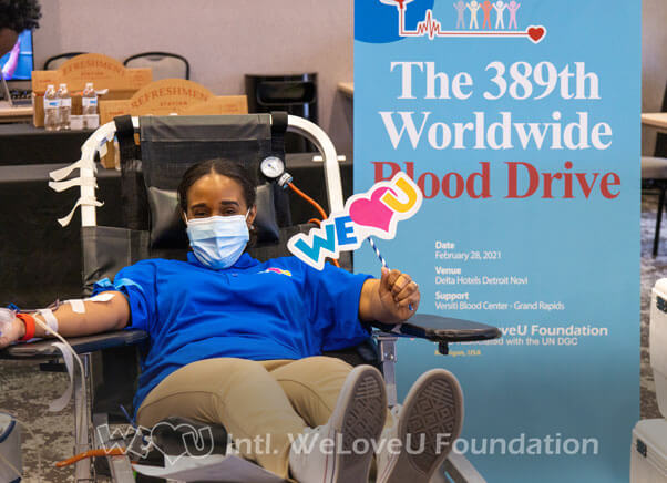 A person donating blood and holding a WeLoveU photo prop