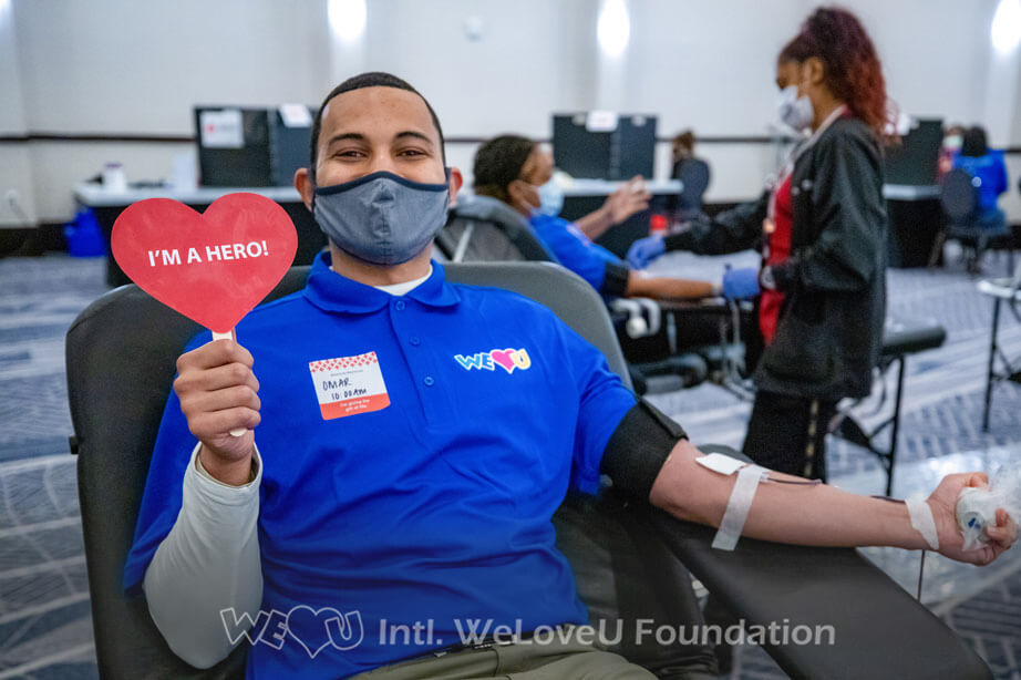 A volunteer donating blood holds up a sign that says 'I'm a hero!'