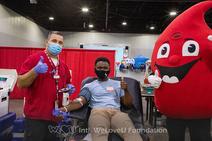 A phlebotomist, blood drop mascot, and blood donor flah a thumbs up at the WeLoveU blood drive
